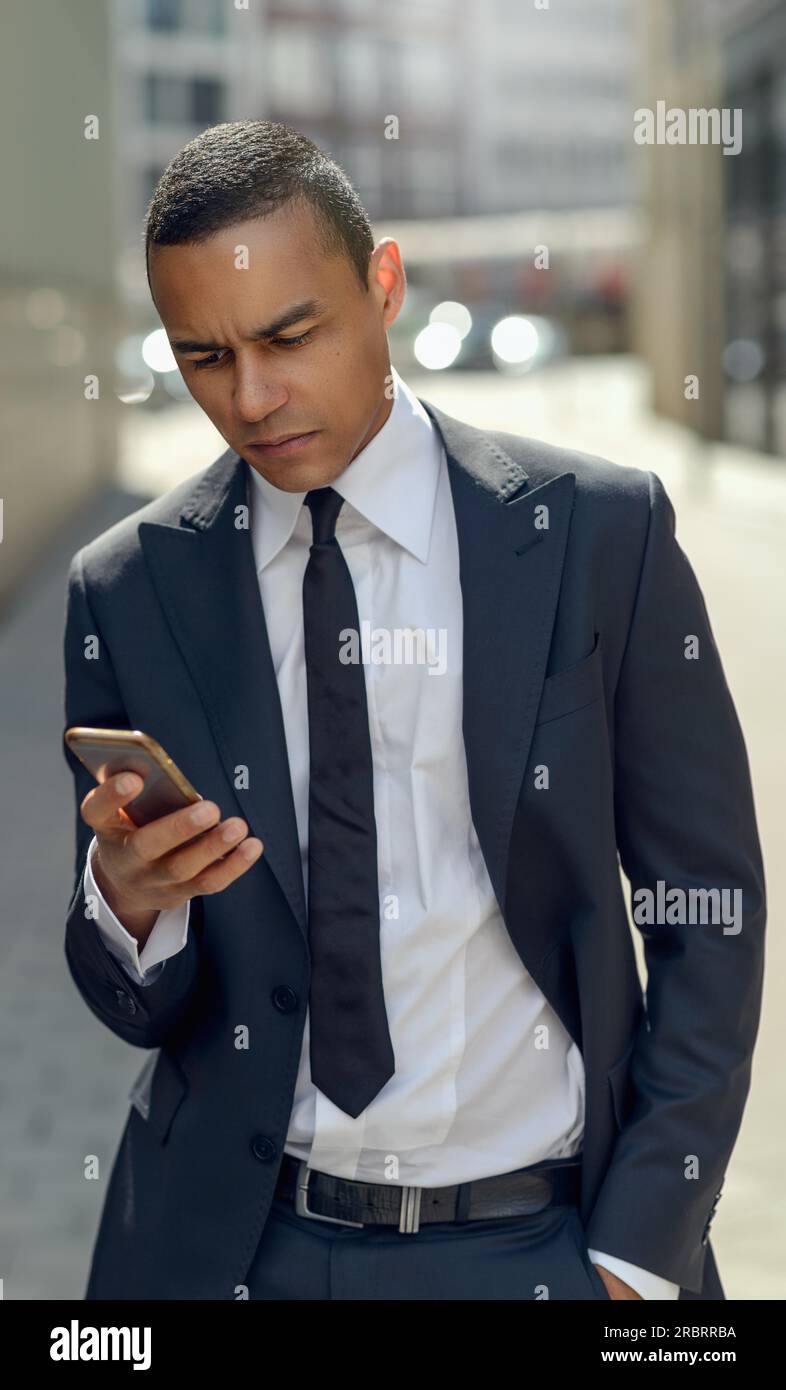 Mezzo Corpo colpo di un giovane imprenditore qualcuno di messaggistica sul suo telefono cellulare mentre si cammina per la strada Foto Stock