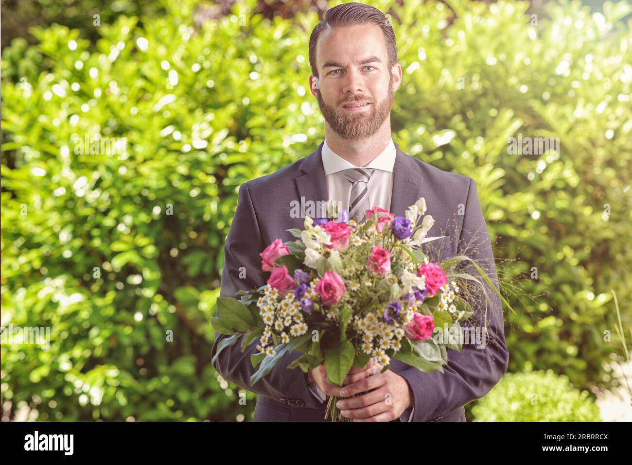 Bell'uomo barbuto con un vestito che porta un bouquet di fiori freschi, forse un pretendente o un beau che chiama un appuntamento, San Valentino, un anniversario Foto Stock