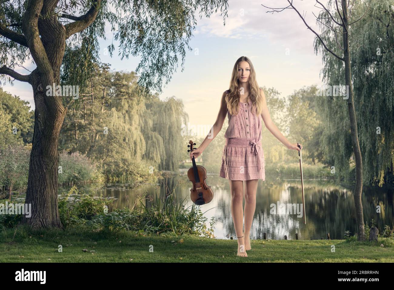 Giovane musicista donna che tiene il suo violino, in piedi vicino al lago e guarda la camera Foto Stock