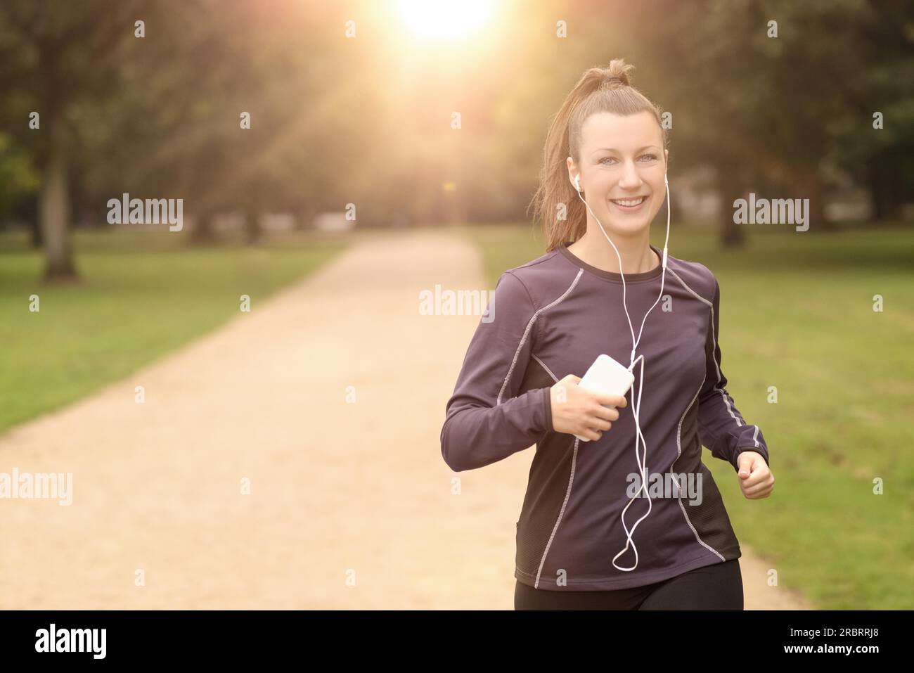 Mezzo Corpo colpo di una bella donna atletica Jogging al parco con le cuffie e sorridente alla fotocamera, con spazio di copia Foto Stock