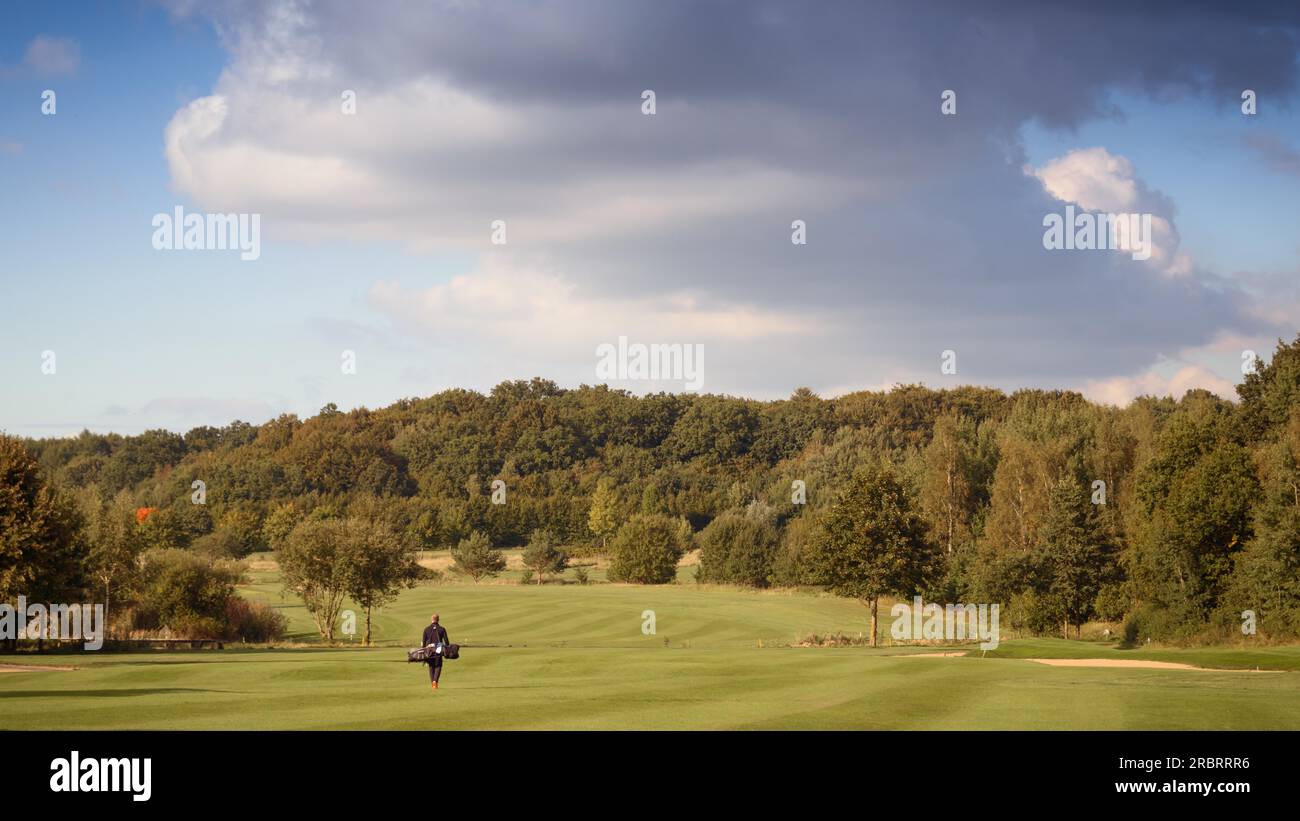 Il Golfer portando una sacca da golf attraverso il fairway su un campo da golf durante una partita di golf, vista del paesaggio di verde e lussureggiante corso Foto Stock