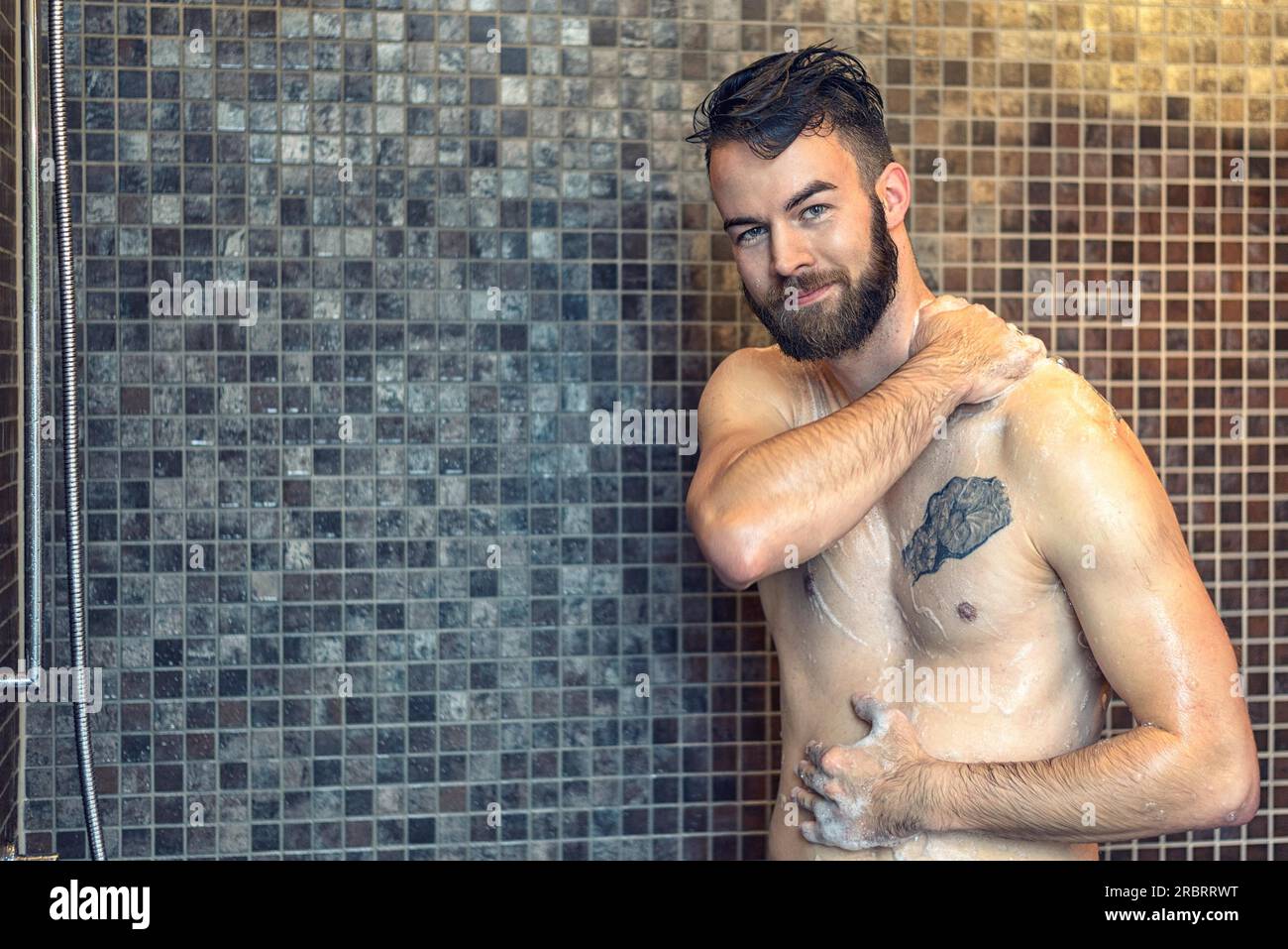 Giovane uomo amichevole con una barba piena che si immerge nella doccia e sorride davanti alla fotocamera, corpo superiore con spazio per le copie Foto Stock