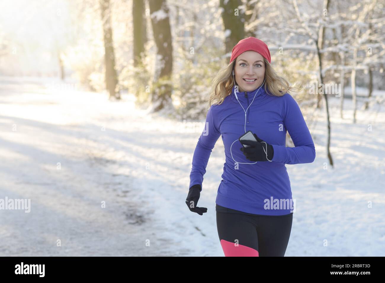 Foto a metà corpo di una bella donna atletica che fa jogging in inverno con auricolari e abbigliamento invernale, sorridendo alla fotocamera, con spazio fotocopie Foto Stock