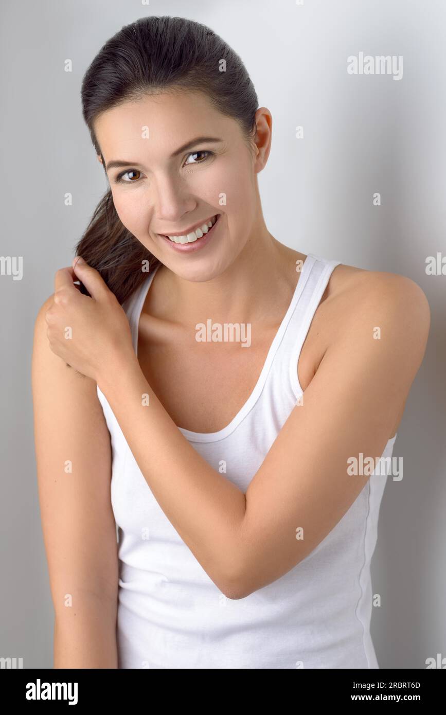 Single carino donna in camicia senza maniche ponytails tiene nelle sue mani mentre sta in piedi vicino al muro grigio Foto Stock
