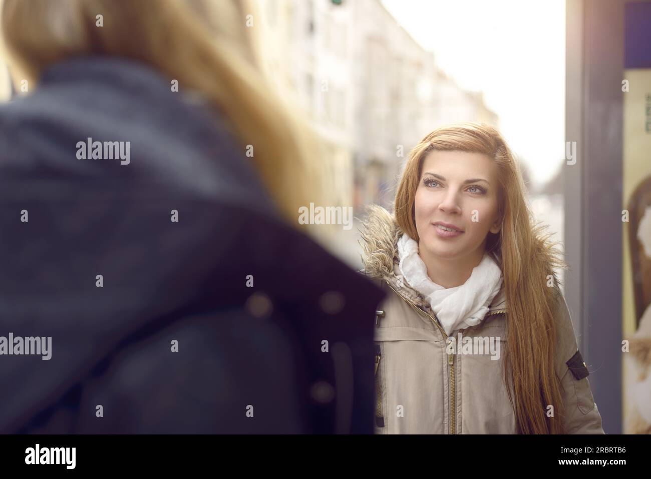 Attraente giovane donna bionda a conversare con un amico femmina all'aperto su una strada urbana di sorridere quando lei ascolta il suo parlare Foto Stock