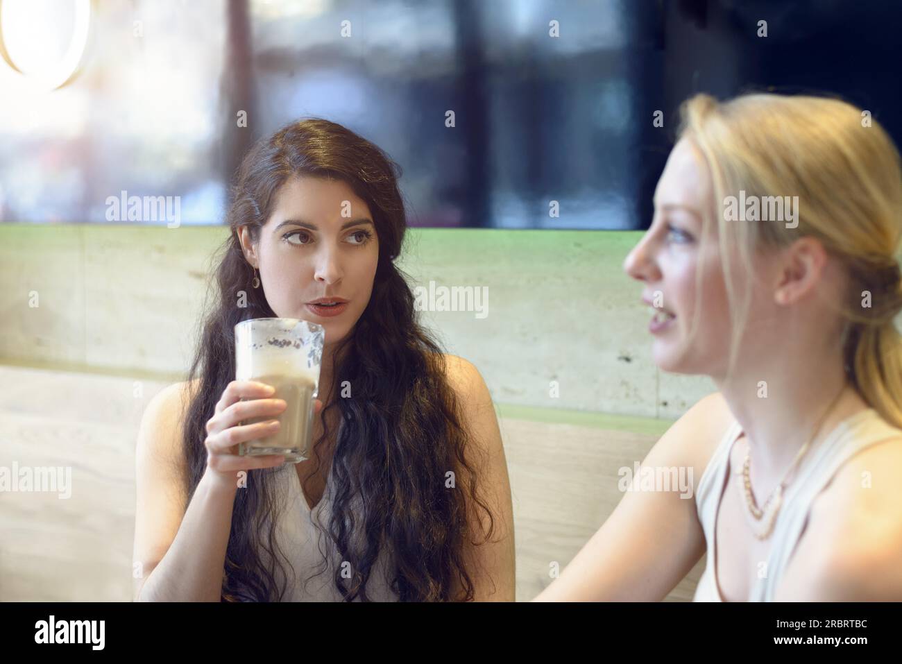Attraente sorridenti giovane donna a chiacchierare con il suo amico come essi siedono ad un tavolo gustando un drink insieme a un ristorante Foto Stock