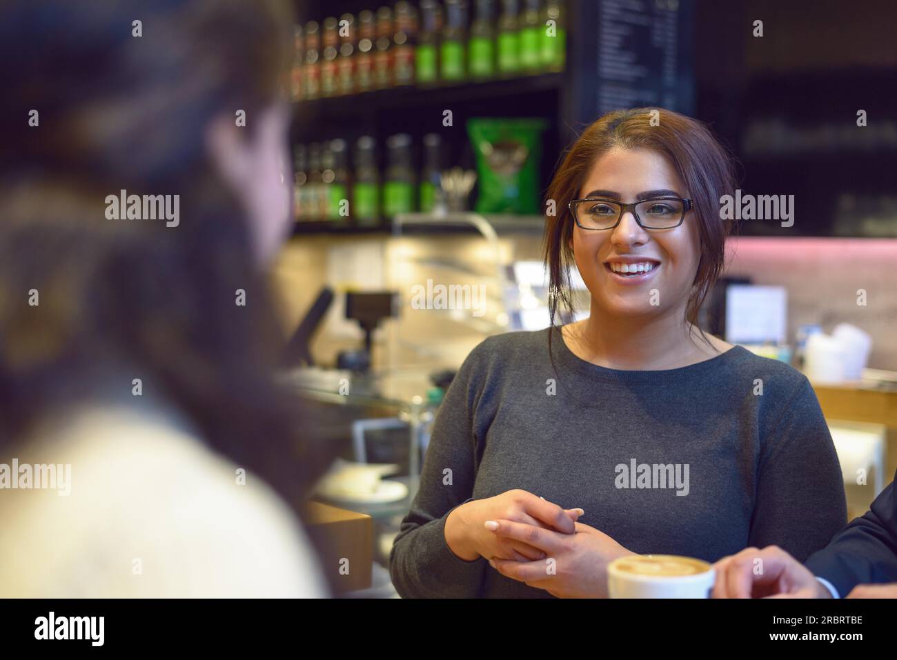 Una giovane cameriera che serve una tazza di caffè a una giovane cliente donna in un ristorante o in un pub che mette la tazza sul tavolo con un sorriso Foto Stock