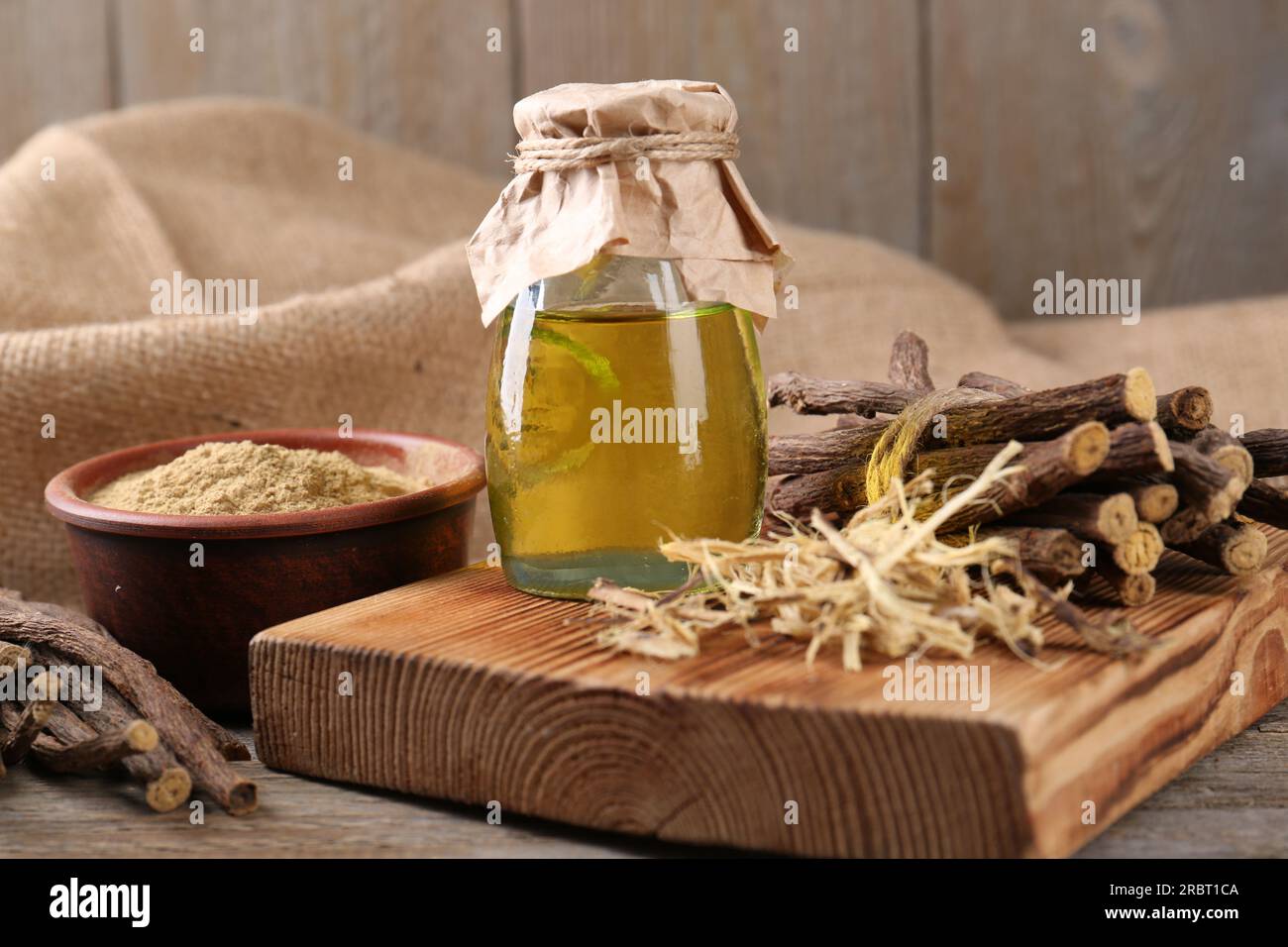 Bastoncini secchi di radice di liquirizia, polvere e olio essenziale su tavola di legno Foto Stock