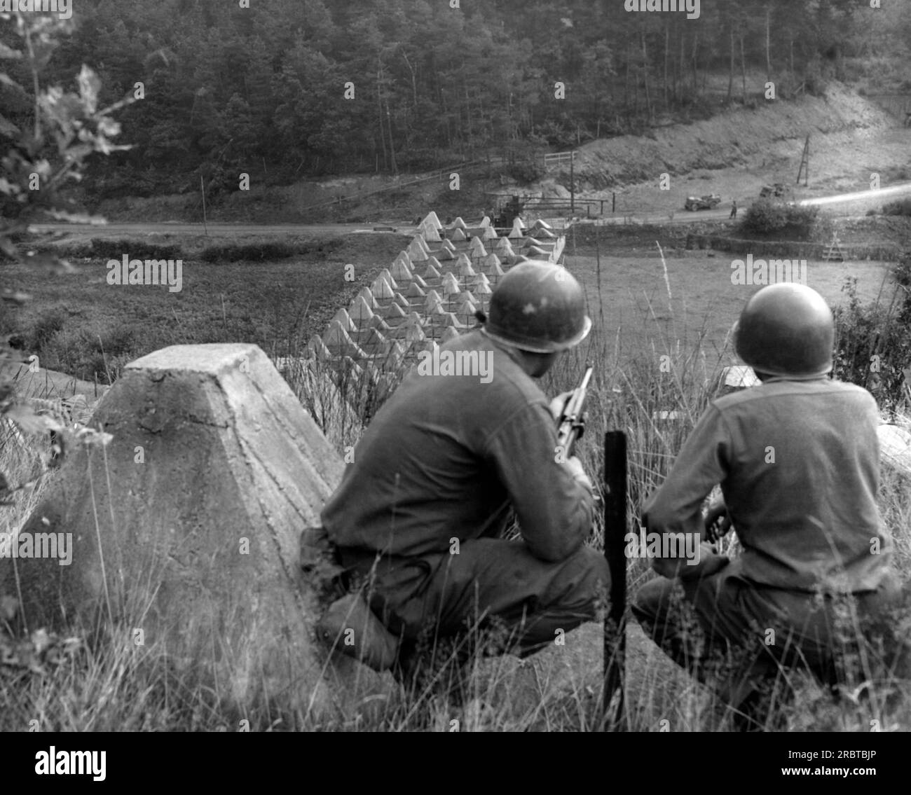 Germania, 1944 due soldati americani che guardano in basso una lunga fila di "denti di drago" dispositivi in cemento per fermare i carri armati invasori alle linee Sigfrido. Foto Stock