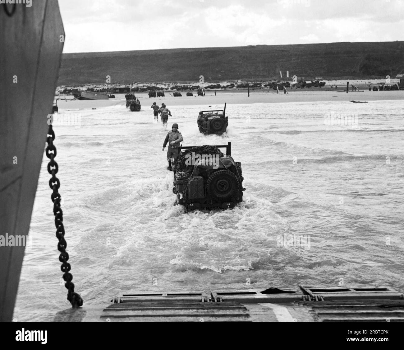 Francia: 9 giugno 1944 soldati alleati fanno una corsa verso la spiaggia, seguiti da jeep, mentre le forze invasori vengono sgogliate dalle navi da trasporto lungo la costa francese. Foto Stock