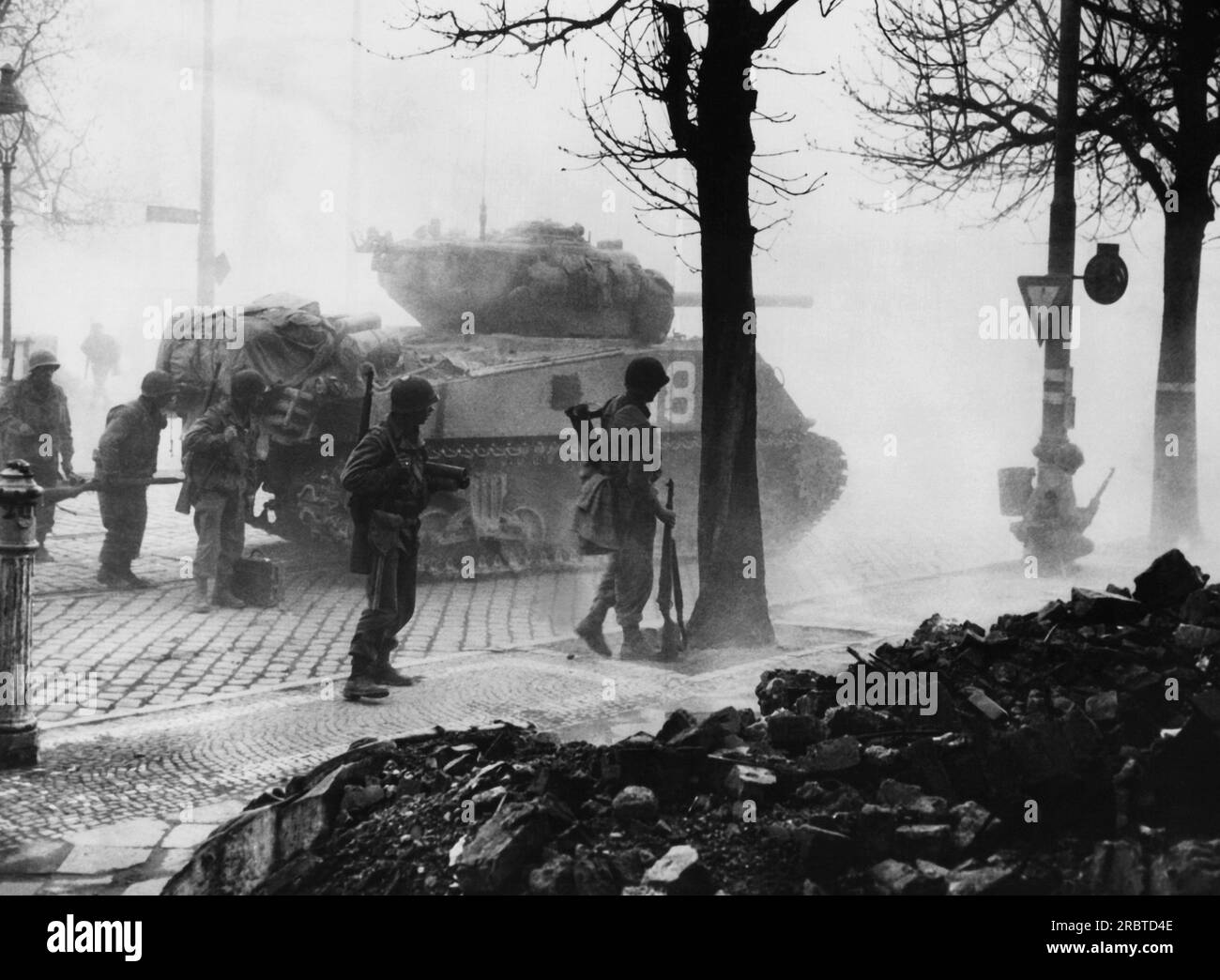 Francoforte, Germania, 7 aprile 1945 i fanti corazzati della terza Armata americana prendono copertura dietro un carro armato che sparava nella città industriale di Francoforte. Il fumo e la polvere provenienti dai proiettili esplosivi danno uno schermo protettivo a Yanks che attendono la parola per assaltare la città. Foto Stock