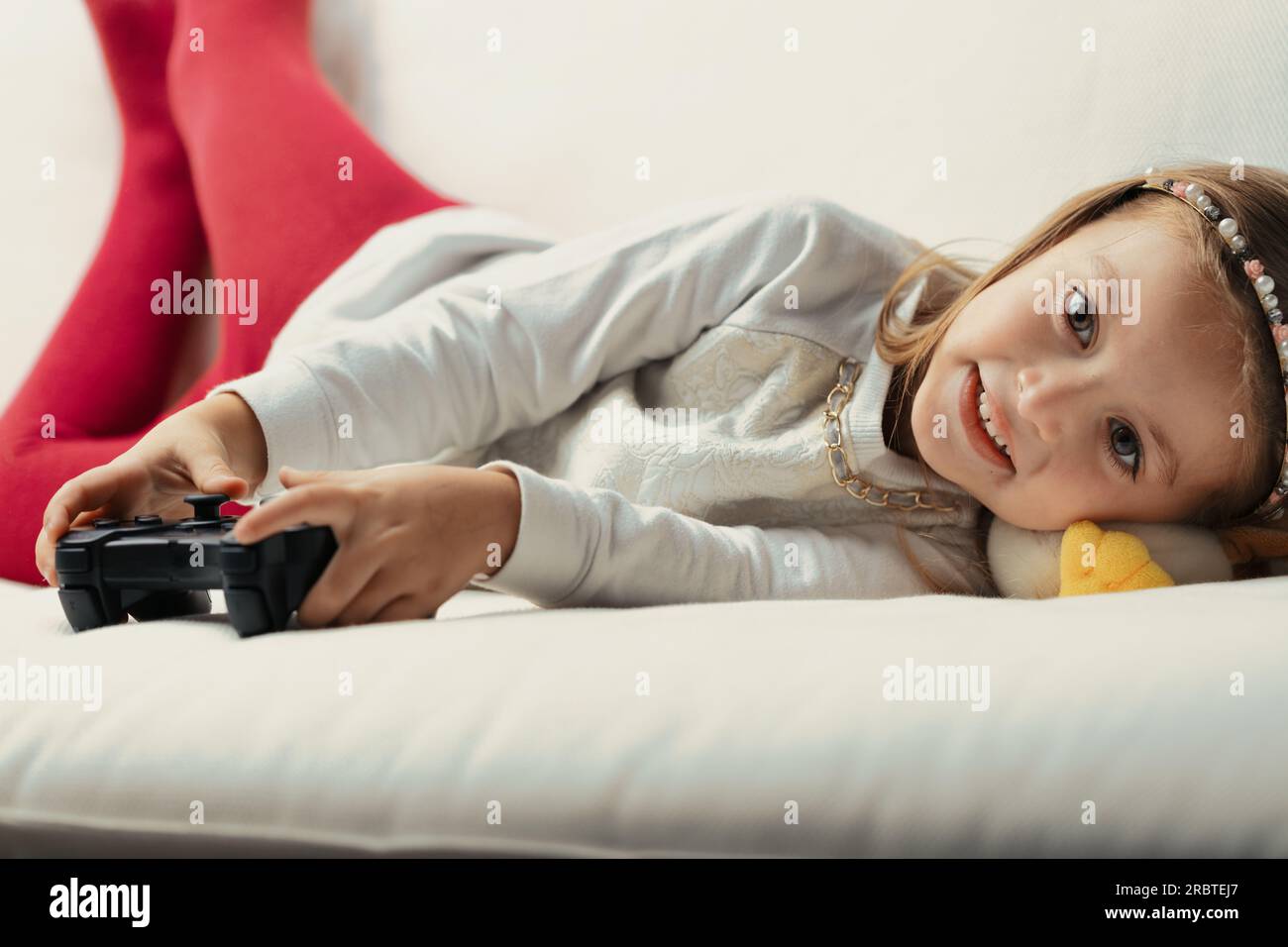 Bambina che gioca a casa sul divano, che si diverte in una sfida emozionante sotto la supervisione dei genitori Foto Stock