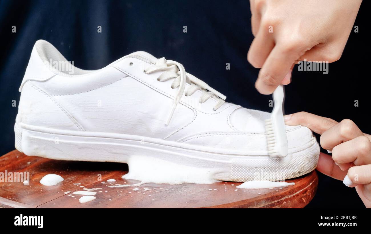 Donna che pulisce scarpe in pelle bianca con schiuma detergente. Il concetto di prendersi cura delle calzature in pelle Foto Stock