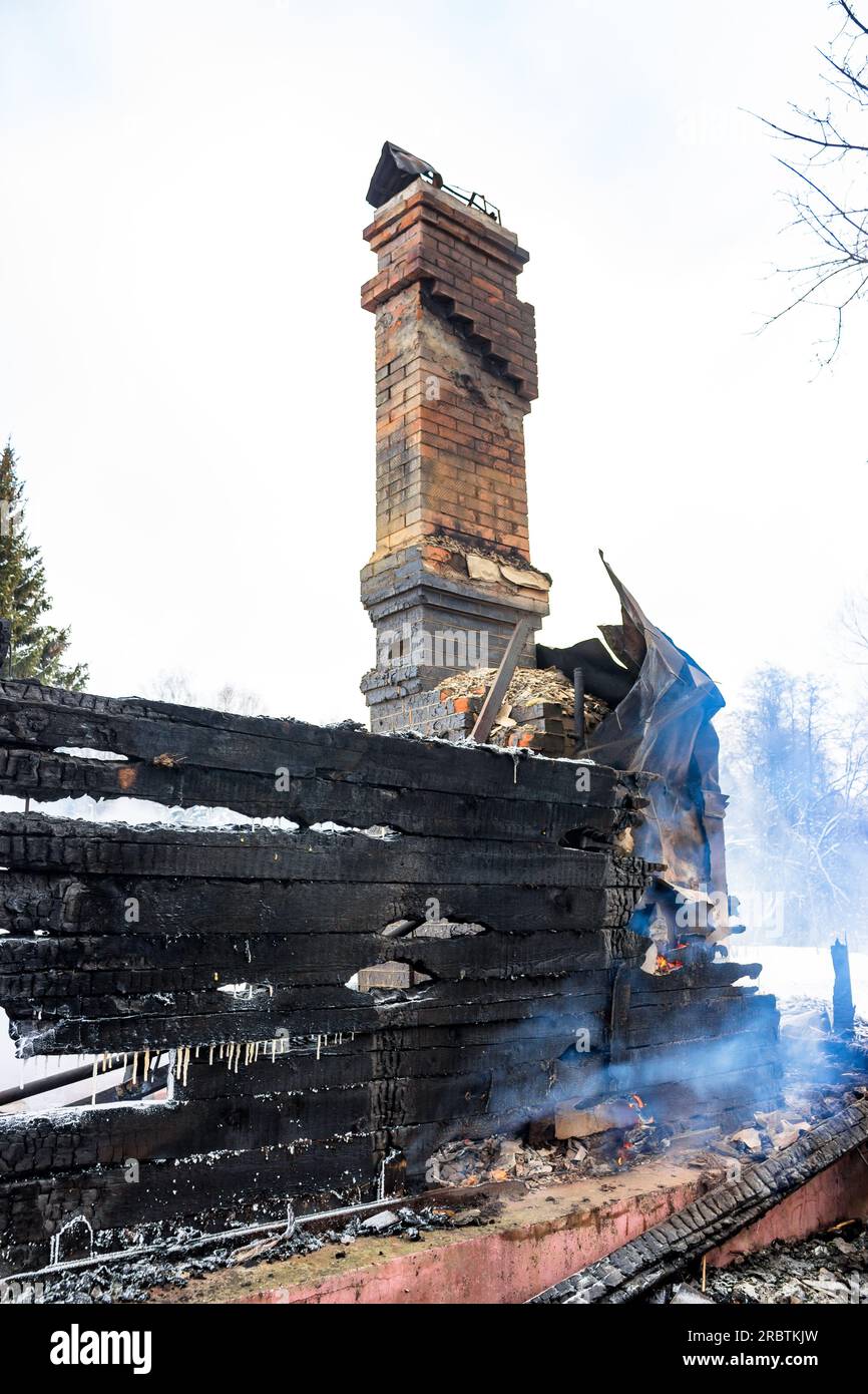 Resti di una casa dopo un incendio. Il tubo in mattoni della stufa è protetto da fumo denso. Una vista verticale della cenere cupa Foto Stock
