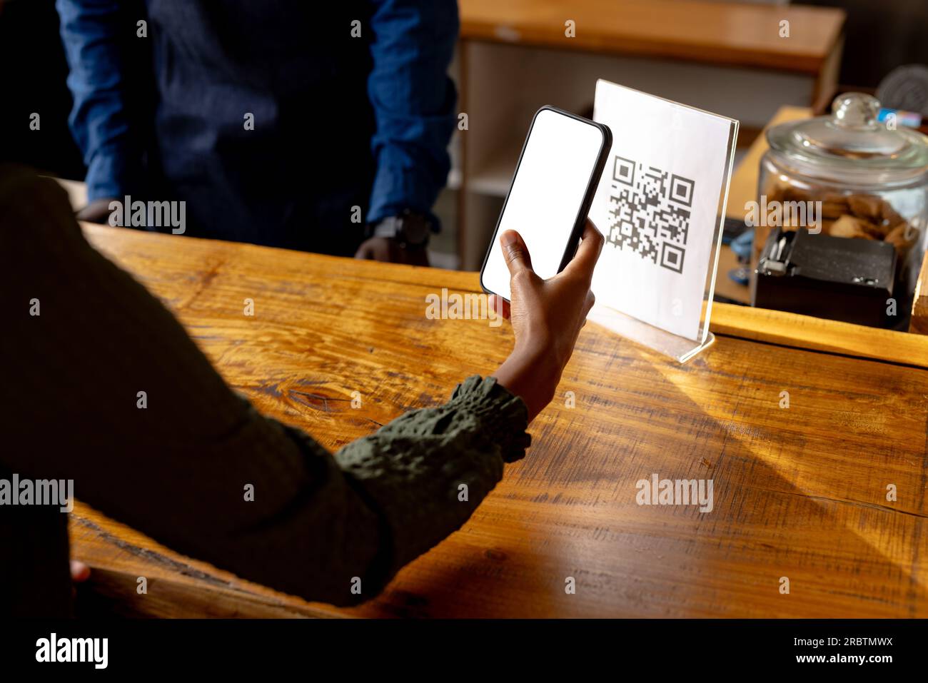 Mano di donna afroamericana che esegue la scansione del codice qr utilizzando lo smartphone in caffetteria Foto Stock