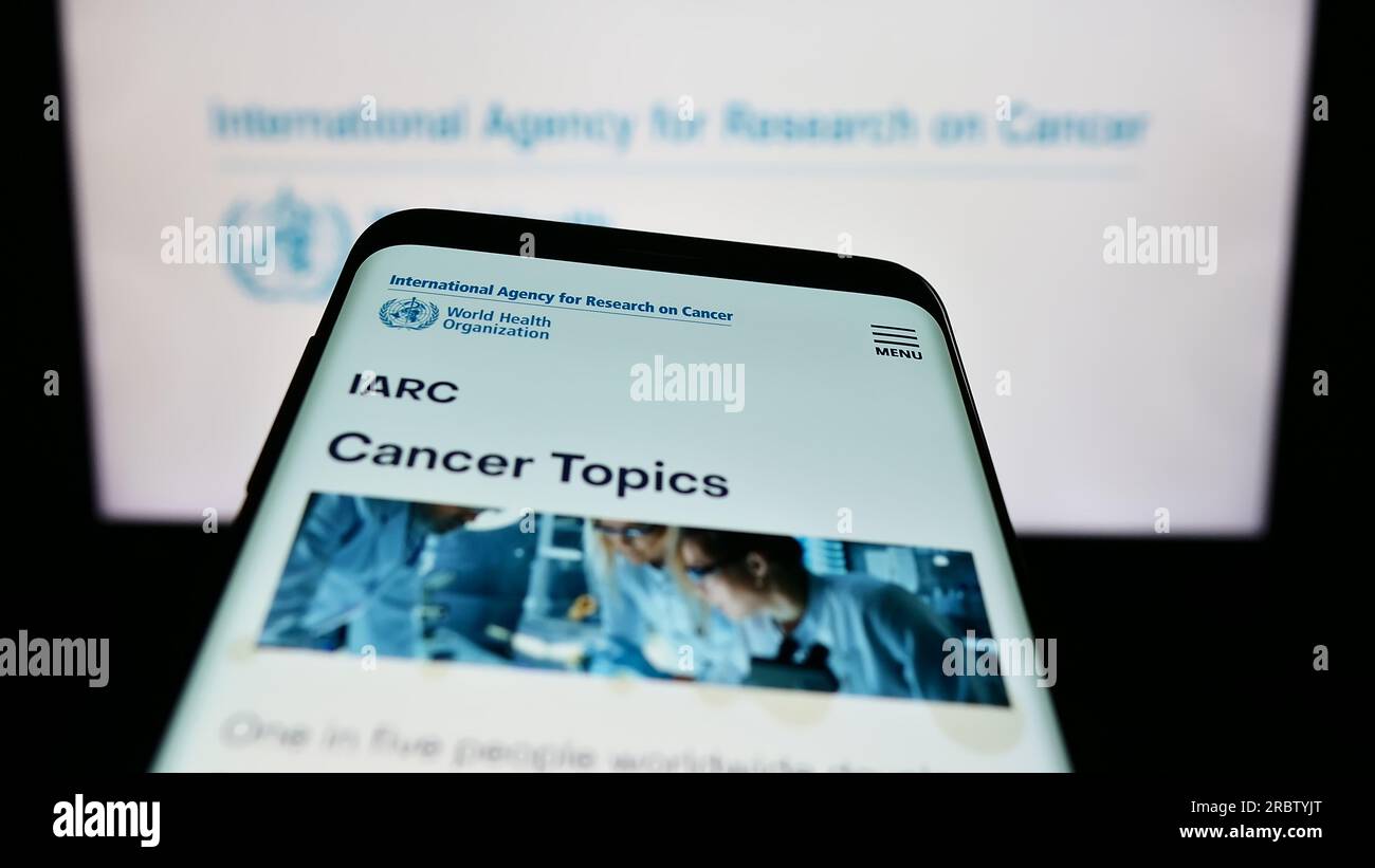 Smartphone con sito Web dell'Agenzia internazionale per la ricerca sul cancro (IARC) sullo schermo davanti al logo. Mettere a fuoco in alto a sinistra sul display del telefono. Foto Stock