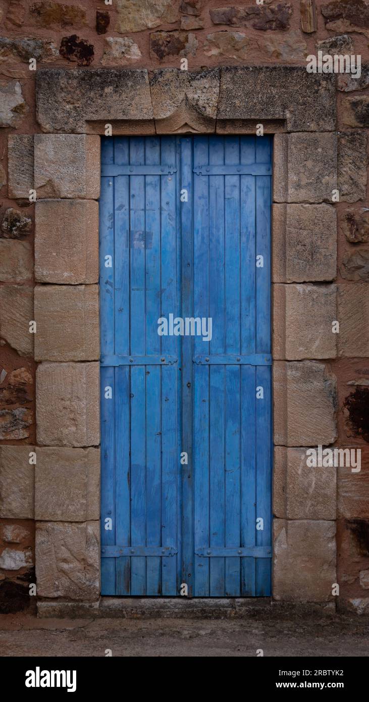 Un vecchio edificio in pietra costruito nel vecchio stile, con una porta in legno con cerniere in ferro dipinte con una sfumatura blu pastello. Foto Stock