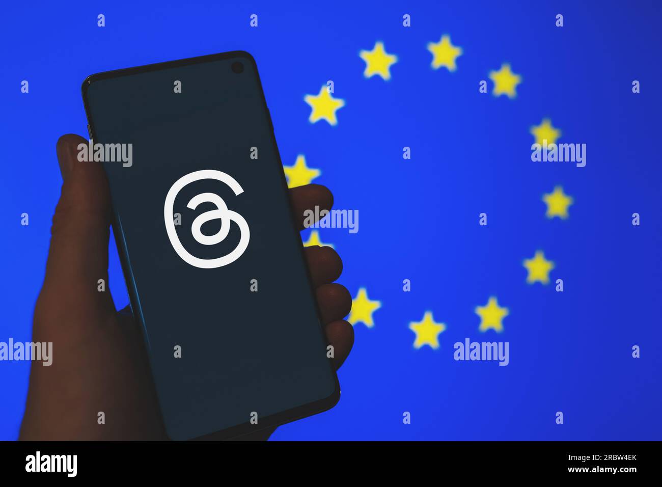 Thread del logo dell'app sullo smartphone in mano con lo sfondo sfocato della bandiera dell'Unione europea. Thread non disponibili in Europa, lancio ritardato Concept. Swansea, Regno Unito - 10 luglio 2023. Foto Stock
