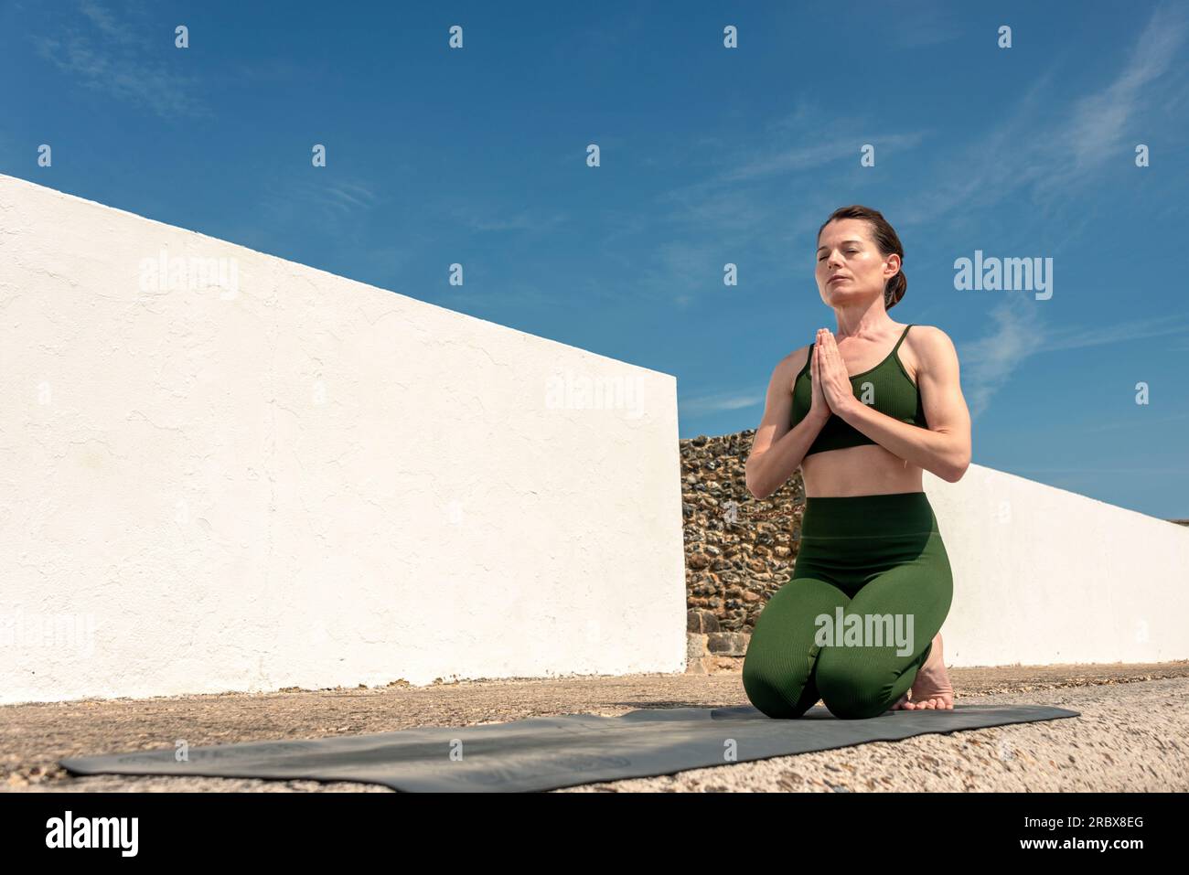 Donna inginocchiata sul tappetino per esercizi che medita fuori al sole Foto Stock