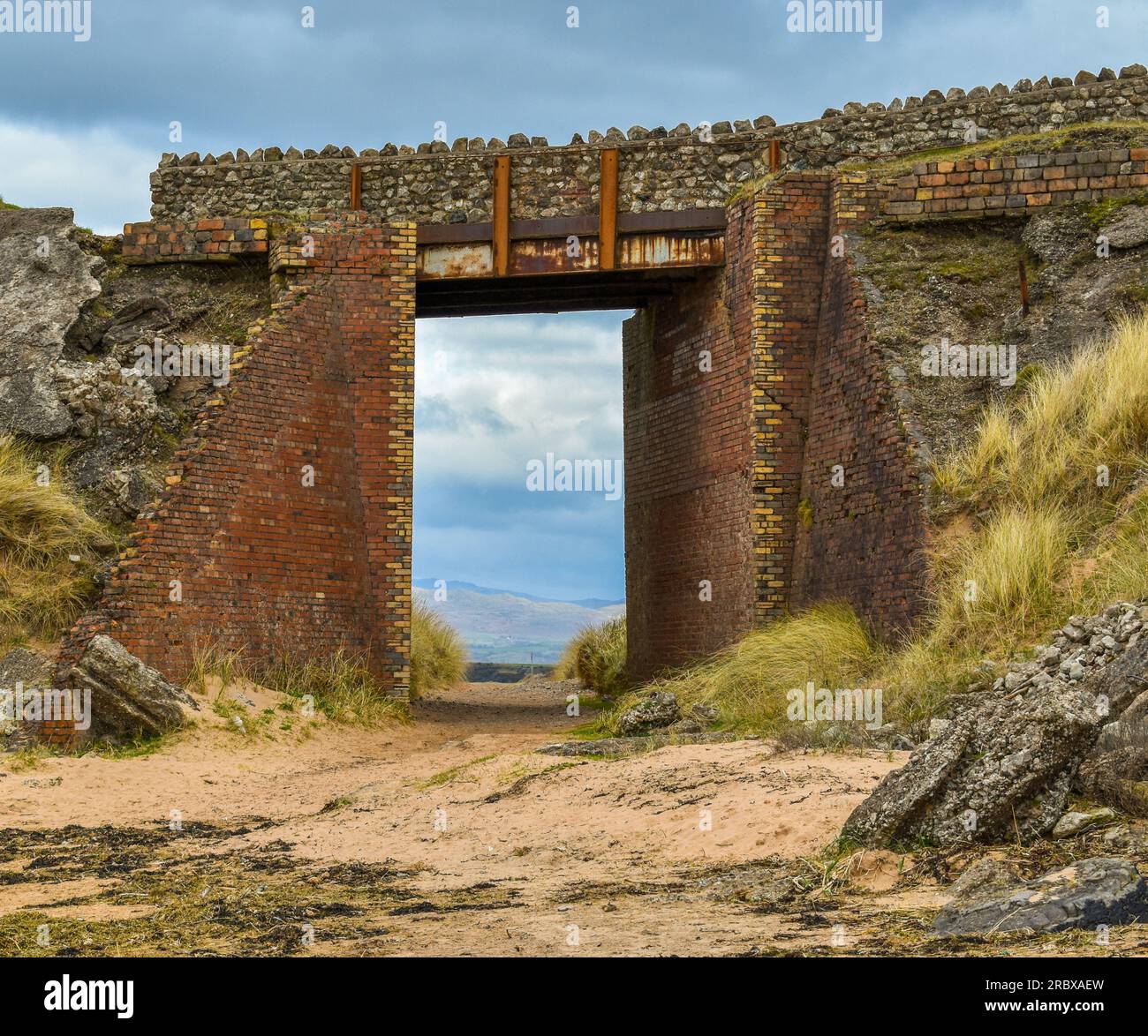 Un vecchio ponte sulla spiaggia con un sentiero sabbioso che vi conduce sotto. Foto Stock