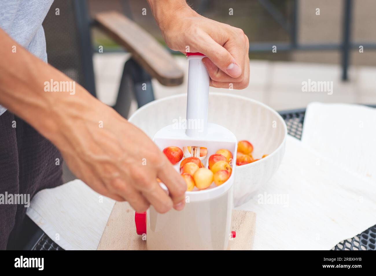 Il lavoratore utilizza un semplice strumento per estrarre pozzi da ciliegie fresche e prepararli per un ulteriore utilizzo. Lavoro manuale con la frutta. Lavori stagionali. Foto Stock