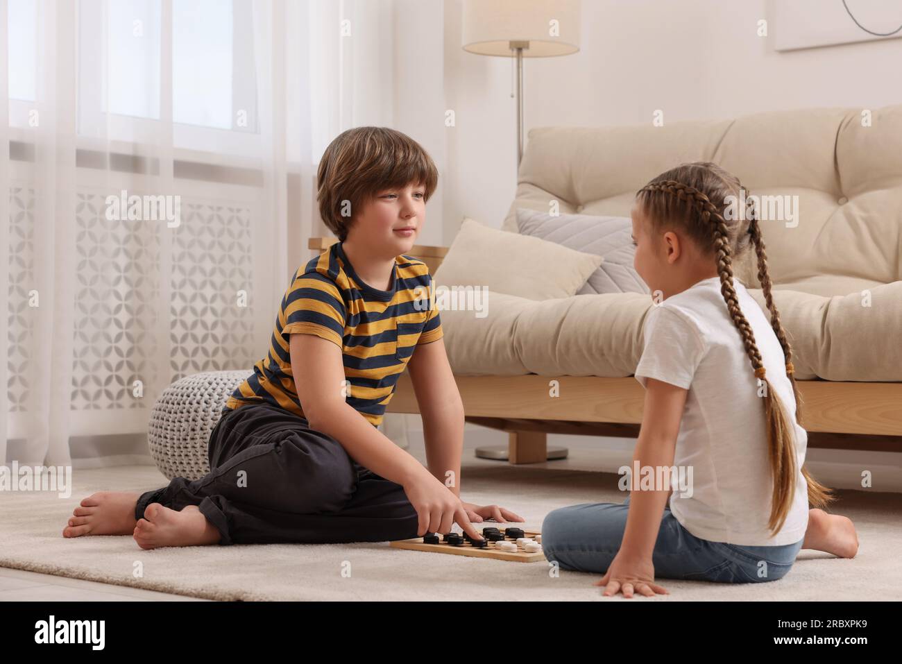 Un ragazzo carino che gioca a dama con una bambina sul pavimento in camera Foto Stock