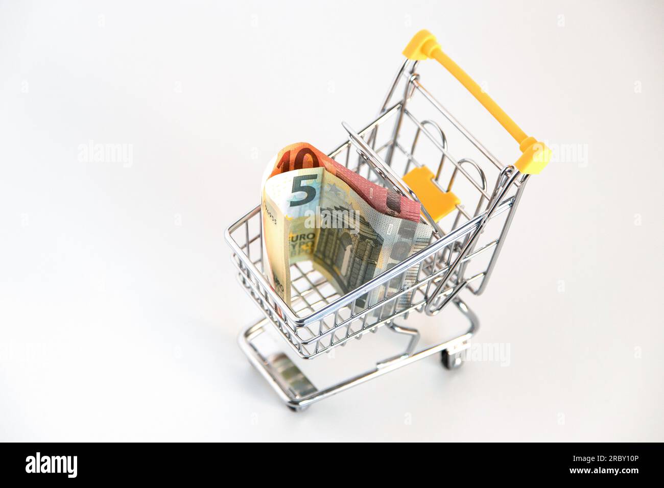 Carrello del supermercato con banconote in euro all'interno su sfondo bianco. Immagine concettuale del potere d'acquisto, delle spese familiari, dei beni essenziali. Foto Stock
