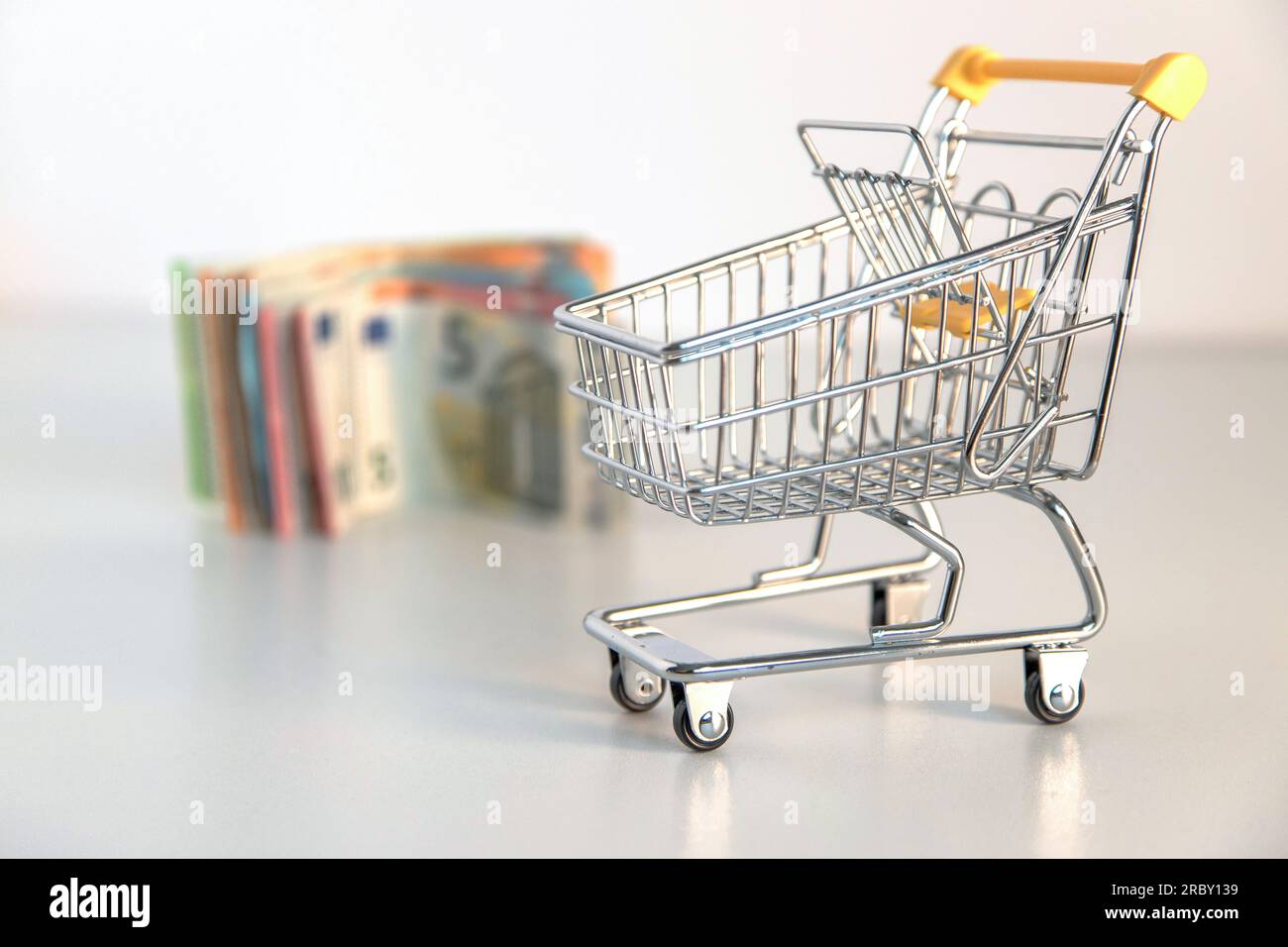 Carrello della spesa vuoto e moneta, diverse banconote in euro su sfondo bianco. Immagine concettuale del potere d'acquisto, delle spese familiari, dei beni essenziali, Foto Stock