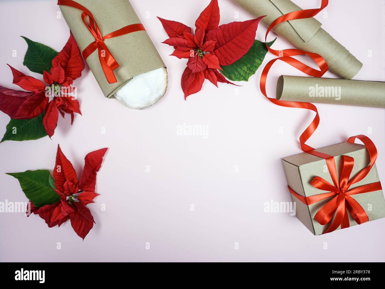 Su uno sfondo rosa, sono esposti gli oggetti per festeggiare il Natale: Uno sgabello di Natale, un regalo, una poinsettia, un nastro per confezionare i regali. Il concetto di Natale. Foto Stock