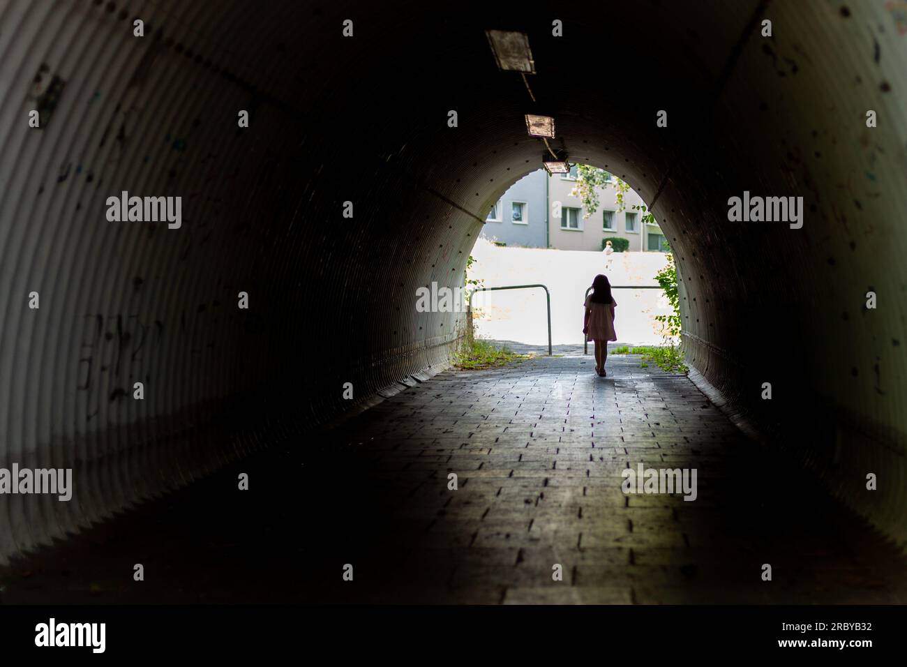 Giovane donna che cammina attraverso un tunnel in città. Vista posteriore. Foto Stock