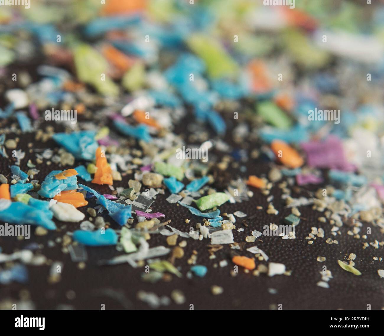 Macro shot su una pila di microparticelle di plastica accanto a un granello di sabbia. Confronto di scala e dimensioni. Foto Stock