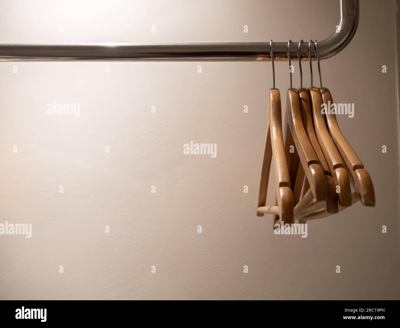 Cinque appendiabiti in legno vuoti senza camicie o abiti appesi a una guida in acciaio nell'armadio di illuminazione soffusa su sfondo bianco con spazio per le copie, preparazione Foto Stock
