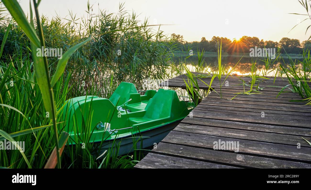 Pedalata legata al molo di legno. Alba sul lago. Paesaggio al lago con canne. Cielo arancione. Foto Stock