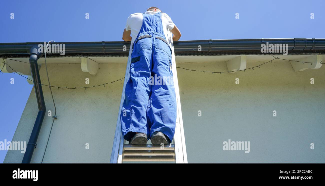 Il tetto della casa ripara il tetto. Il tetto al lavoro. Tetto in piedi sulla scala di metallo. Foto Stock