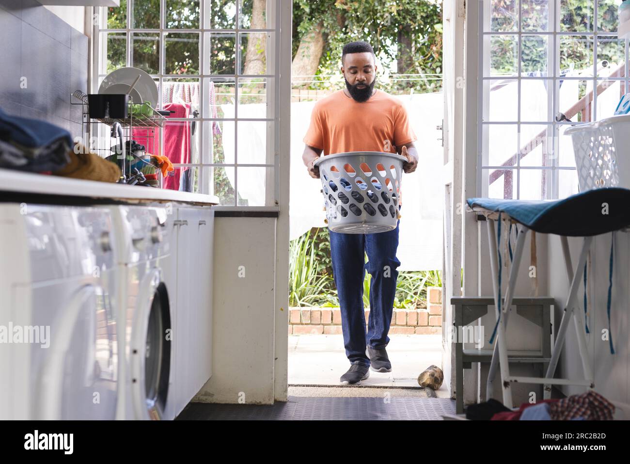 Uomo afroamericano concentrato che cammina con scatola di lavatrici in cucina e lavatrice Foto Stock