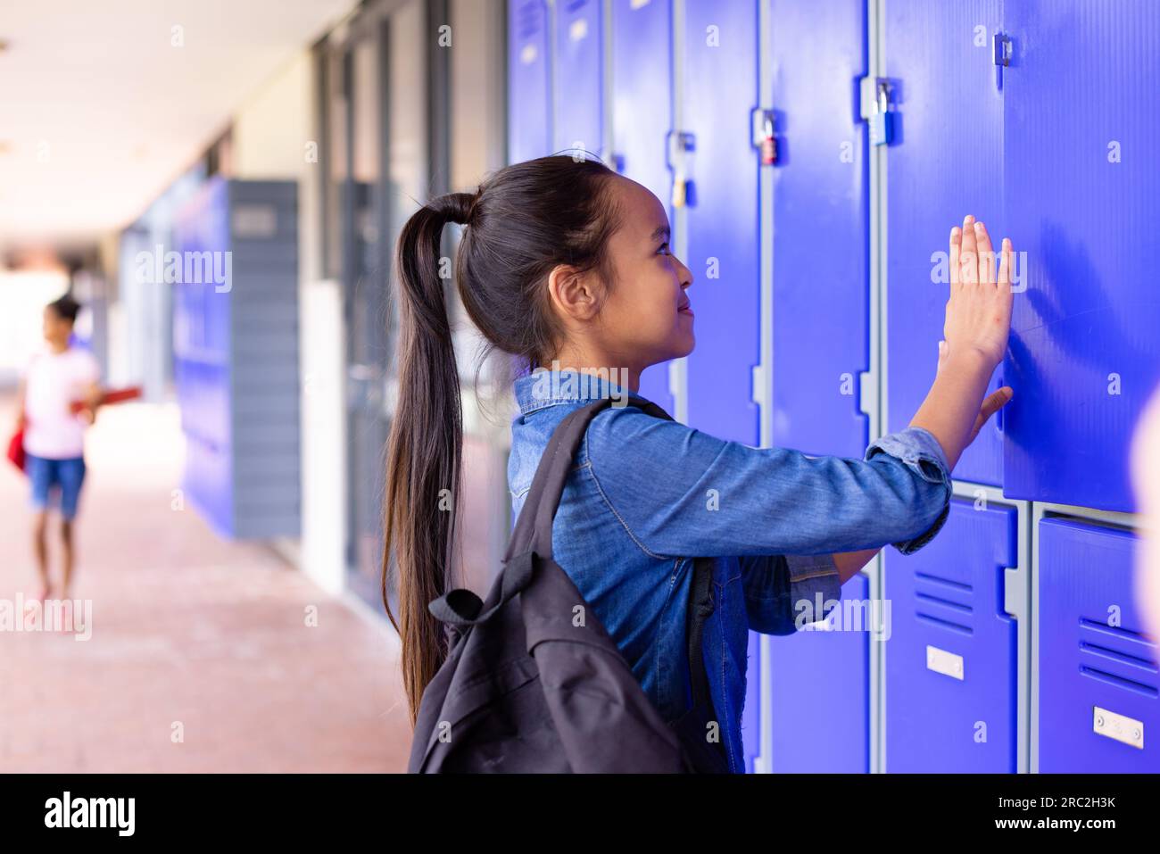 Felice studentessa birazziale in piedi accanto agli armadietti nel corridoio della scuola Foto Stock