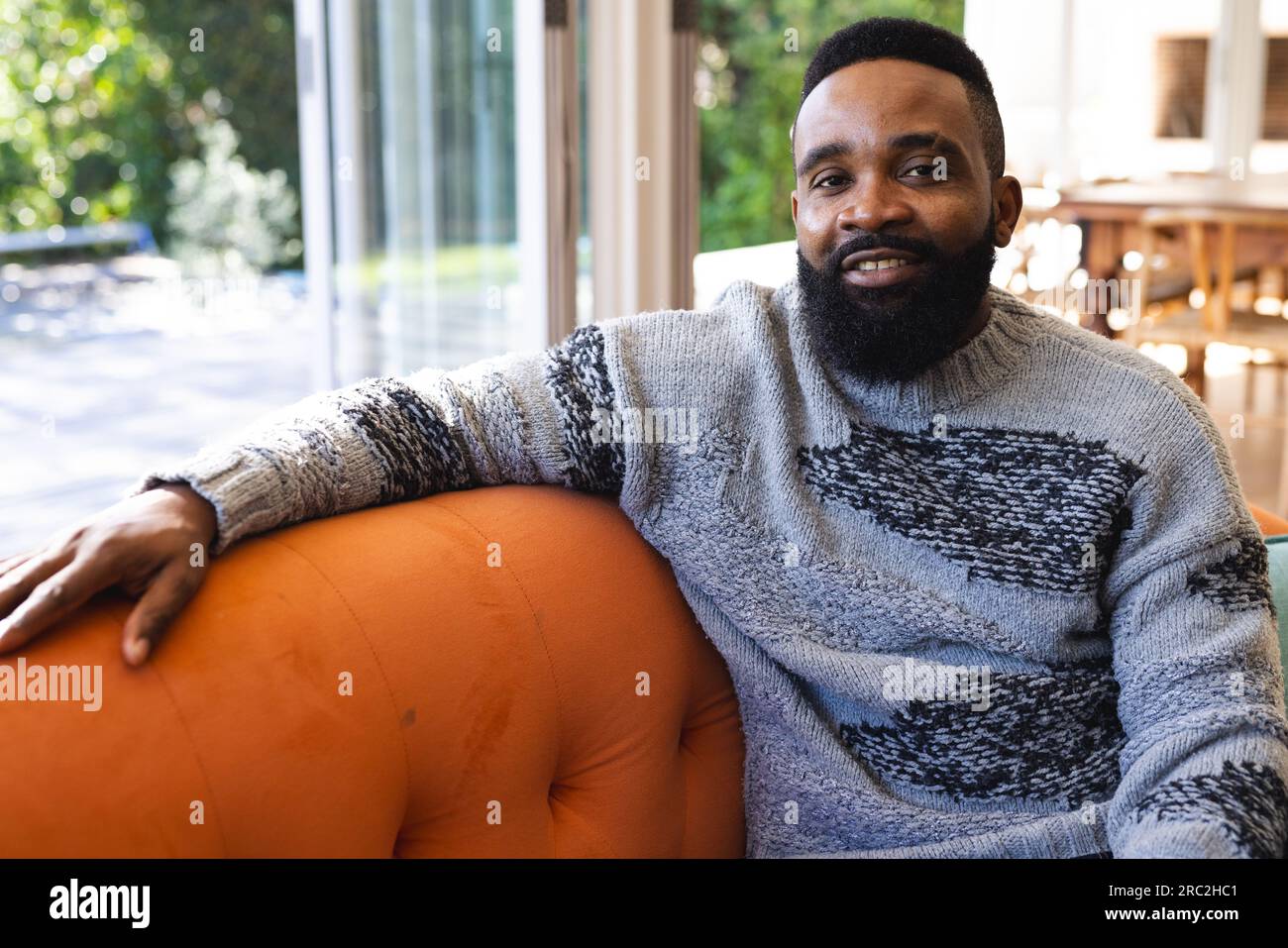 Ritratto di un uomo afro-americano felice che indossa un maglione e si siede sul divano a casa Foto Stock