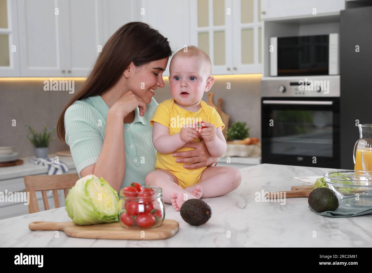 Felice giovane donna e il suo piccolo bambino che cucinano insieme in cucina Foto Stock