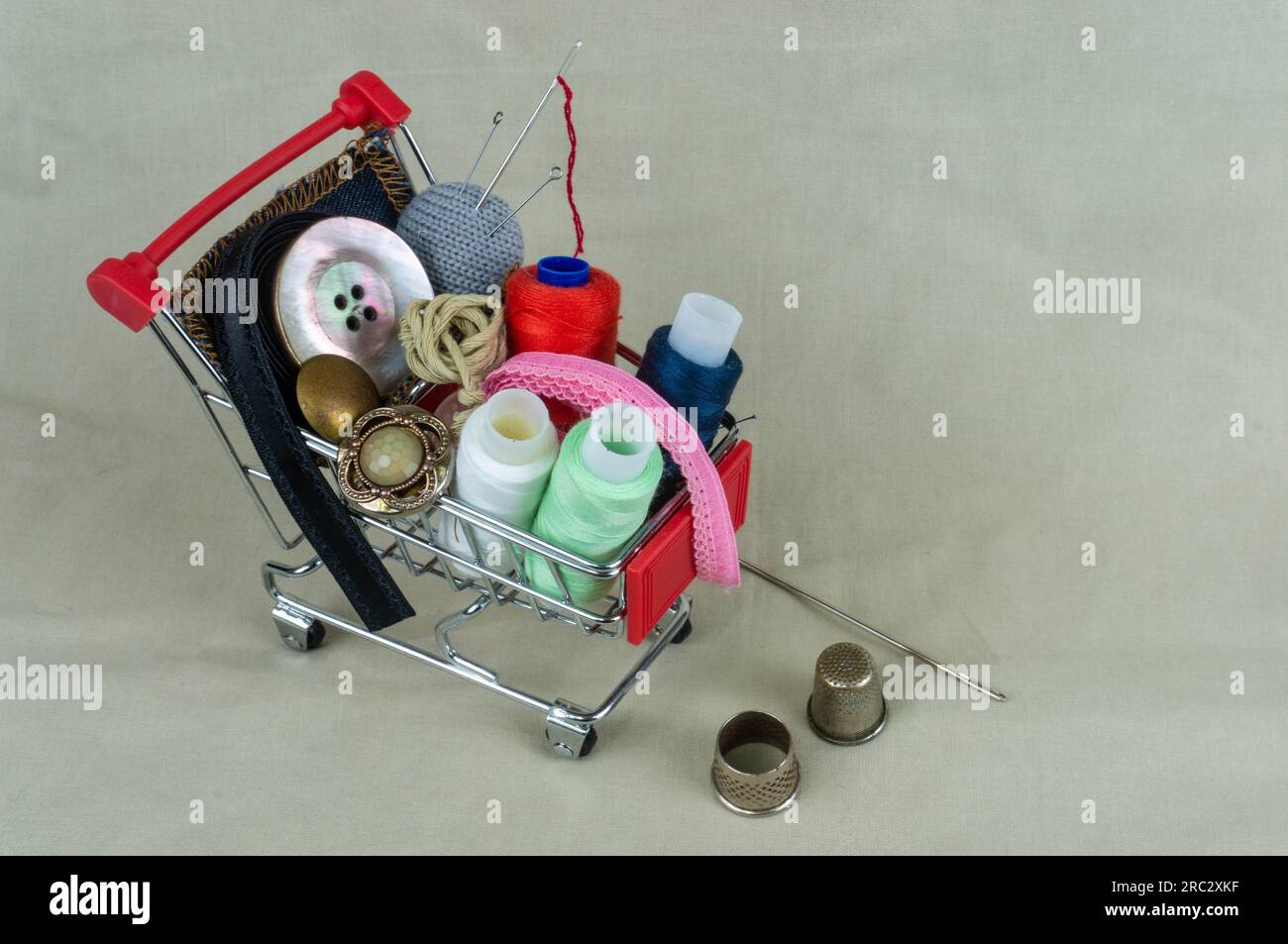 Carrello da officina con fili, accessori per cucire e bottoni. Accanto a ditali e strumenti per cucire e ricamare. Lo sfondo è in grigio-beig Foto Stock