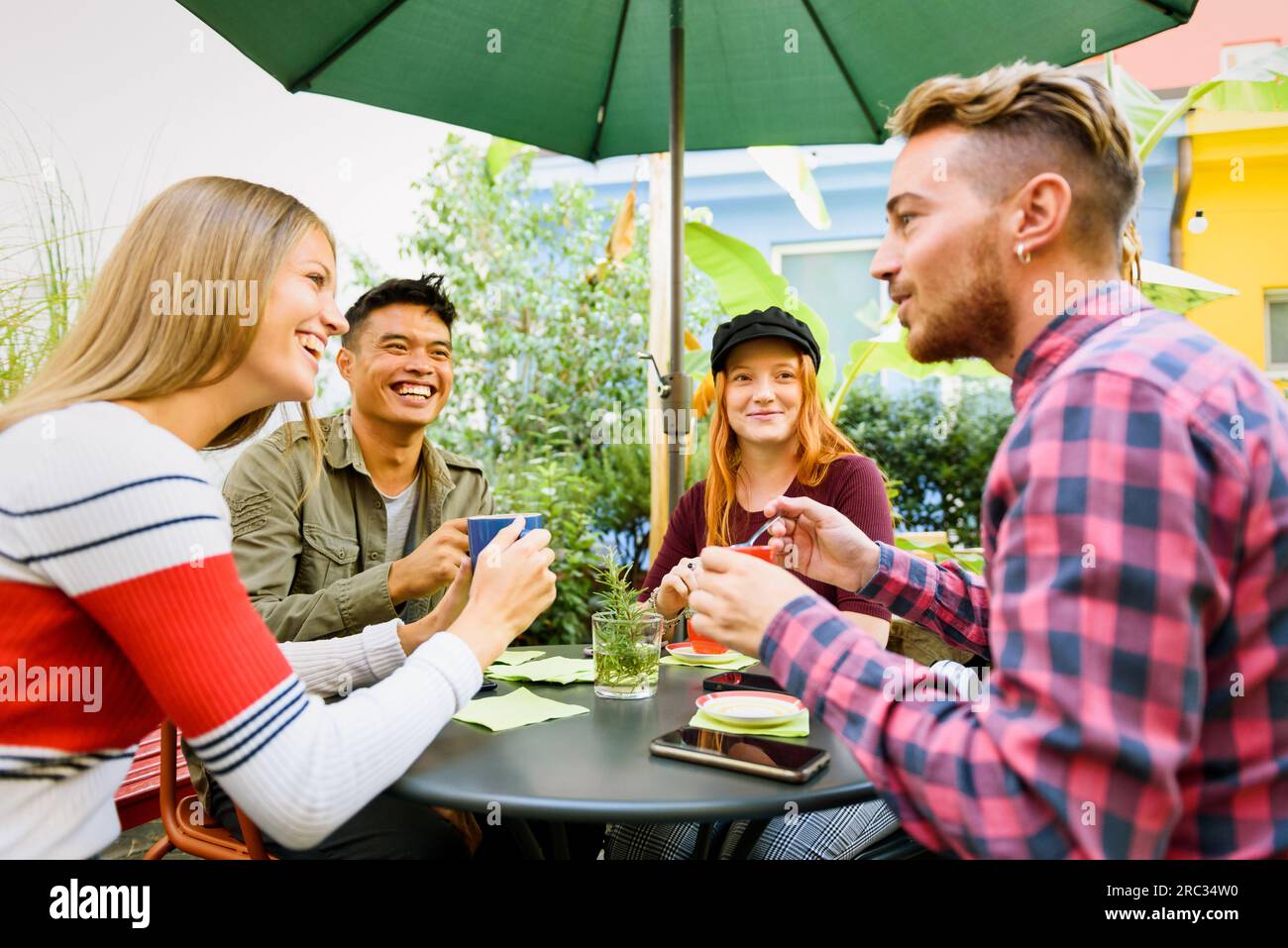 Uomini e donne multirazziali in abiti informali sorridono e parlano tra loro mentre si siedono al tavolo durante la pausa caffè nella caffetteria all'aperto Foto Stock