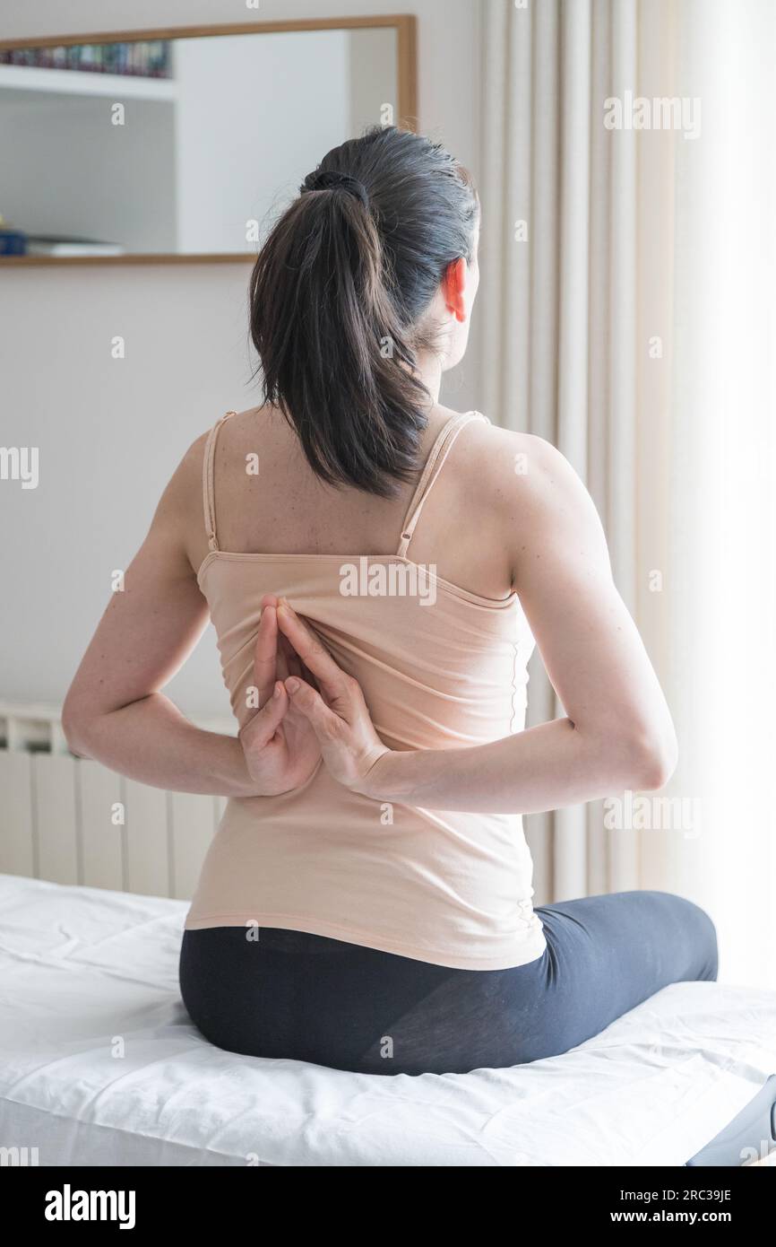 Giovane donna caucasica adulta seduta e di fronte alla schiena facendo esercizi posturali con le mani. Consapevolezza del corpo e concetto di stile di vita. Primo piano. Foto Stock