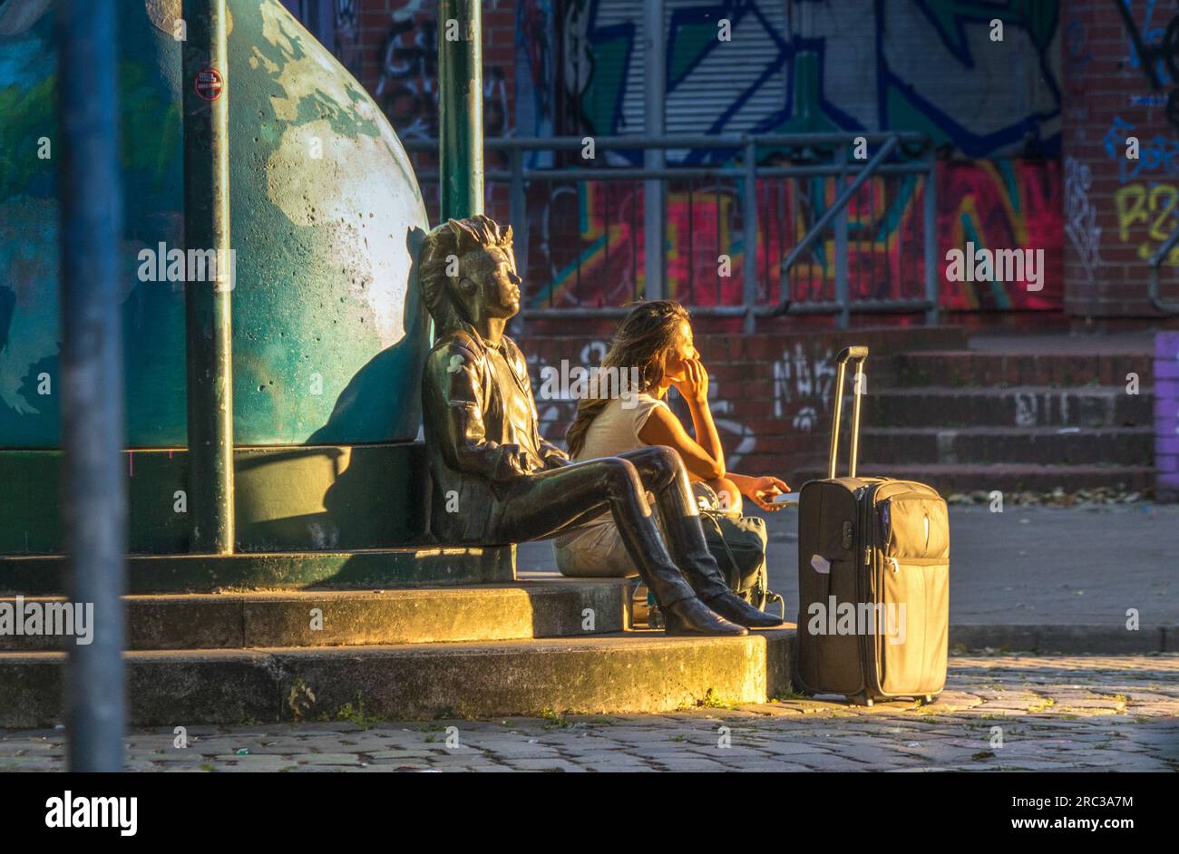 Giovane donna che aspetta seduta accanto alla statua di un punk in Admiralstrasse, Kreuzberg, Berlino Foto Stock