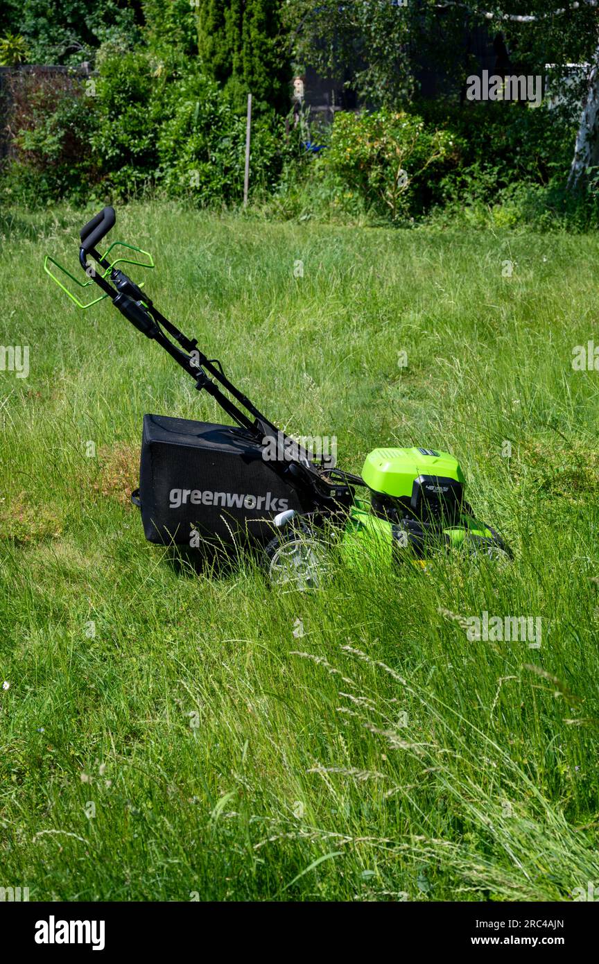Un rasaerba Greenworks che taglia un prato in erba dopo che non è stato tagliato può quando l'erba è lunga. Foto Stock
