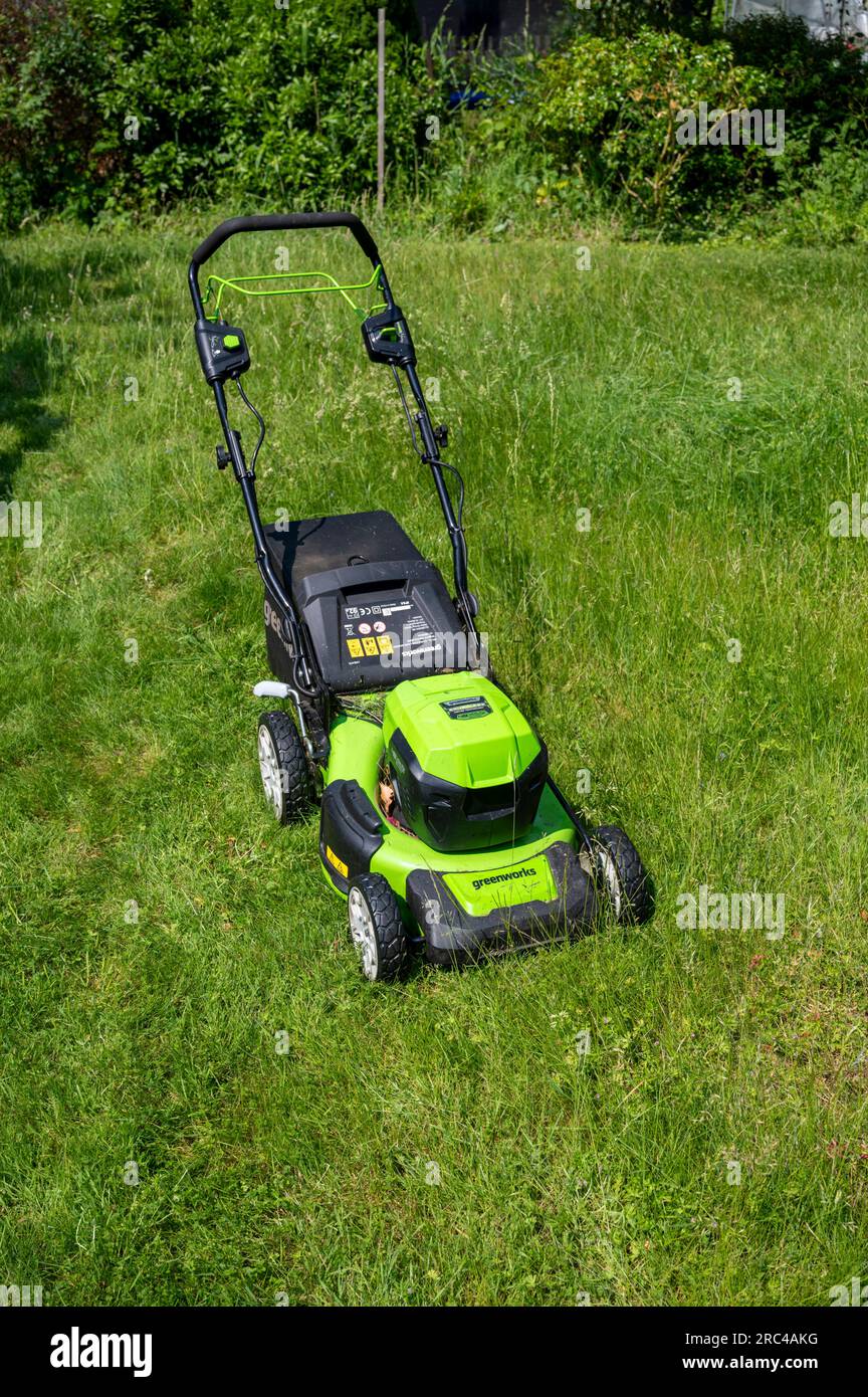 Un rasaerba Greenworks che taglia un prato in erba dopo che non è stato tagliato può quando l'erba è lunga. Foto Stock