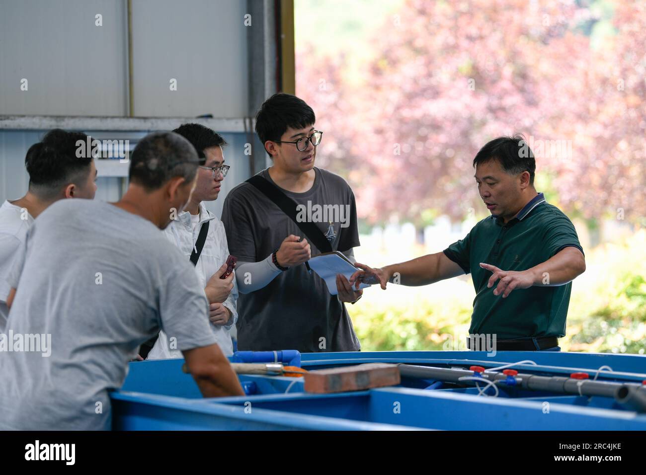 (230712) -- CHENGDU, 12 luglio 2023 (Xinhua) -- Zhou Liang (1st R) parla con gli studenti in visita dalla China Three Gorges University in una base di allevamento gestita congiuntamente dall'Istituto Yibin degli animali acquatici rari e dall'Istituto di pesca dell'Accademia di Scienze agricole del Sichuan a Yibin, nella provincia del Sichuan nel sud-ovest della Cina, il 27 giugno 2023. Zhou Liang, 51 anni, è il direttore del Yibin Institute of rare Aquatic Animals. Ha iniziato a studiare con suo padre il soggetto dell'allevamento artificiale di pesci rari dal 1993. Dopo la riuscita propagazione artificiale del pesce genitore dello storione dello Yangtze si è allevato in Th Foto Stock