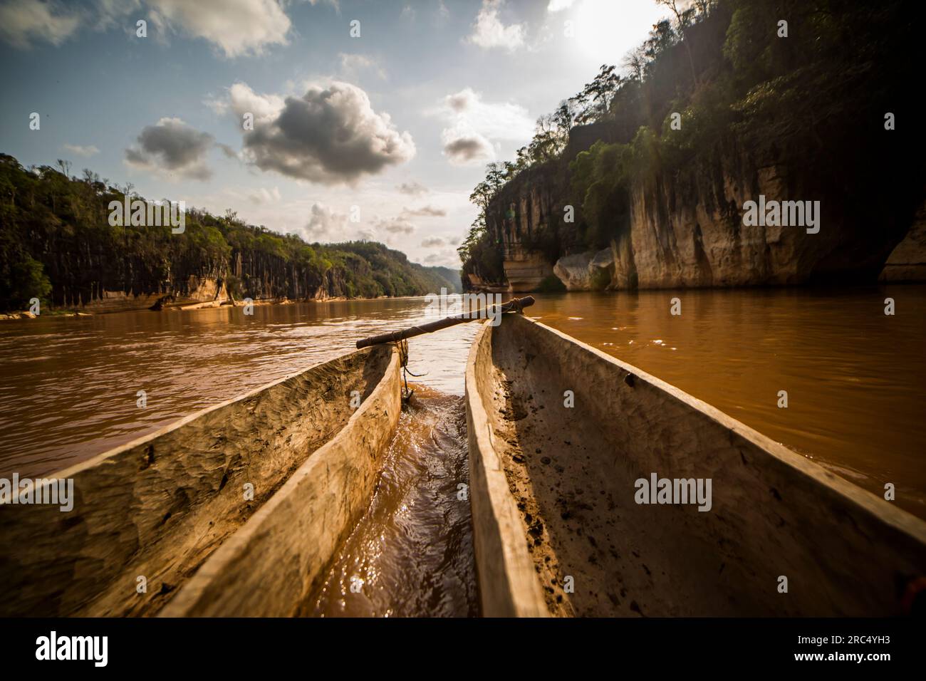 Trasporta barche di legno legate tra loro ad archi con tavola di legno e galleggianti nell'acqua fluente del fiume in Madagascar contro nuvolosi alberi blu cielo verde Foto Stock