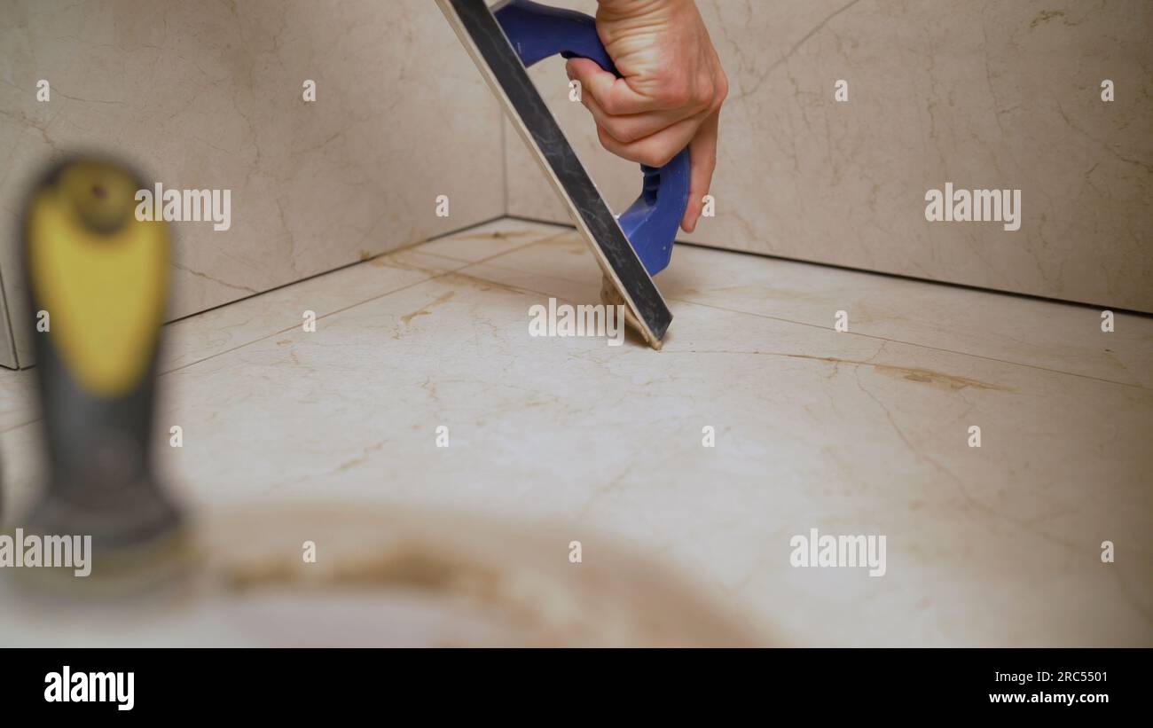 La mano dell'uomo che tiene un galleggiante in gomma e riempie i giunti con Malta. Il lavoratore sta strofinando le piastrelle con un galleggiante. Foto Stock