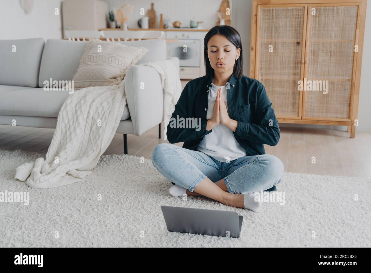La donna calma allevia lo stress, medita in posa di loto a casa. Ascoltare le affermazioni, fare yoga. Stile di vita sano. Foto Stock