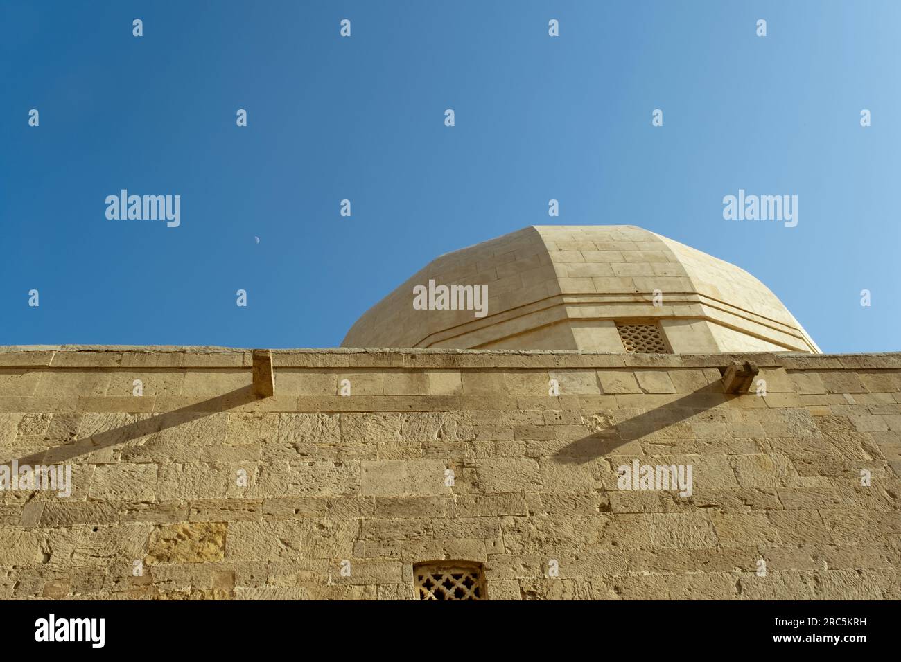 Una fotografia che cattura una storica cupola della moschea a Icherisheher, la vecchia città di Baku, in Azerbaigian, con una vista della luna nel cielo blu. Foto Stock