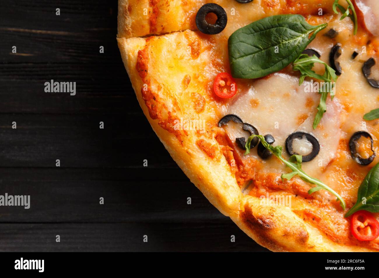 Pizza italiana con jerky, formaggio, olive ed erbe su uno sfondo di legno scuro, vista dall'alto. Foto Stock